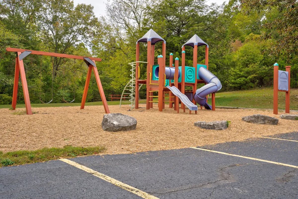 This joyful exterior captures a well-equipped playground surrounded by natural greenery, with children’s swings and climbing structures suggesting family fun and outdoor play.