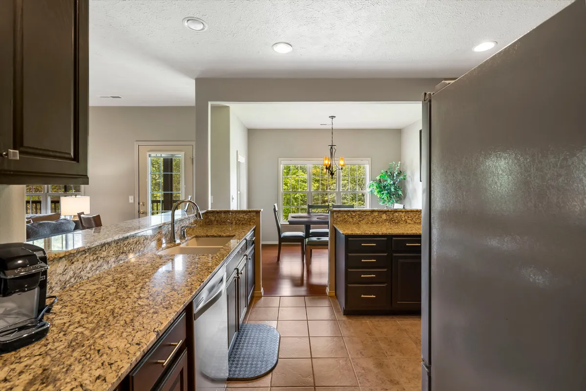 A perspective of the renovated kitchen and dining area, showcasing granite countertops, stainless steel appliances, and a dining table with a view of the fairway. The space is bright and functional, emphasizing both meal preparation and the enjoyment of shared meals.