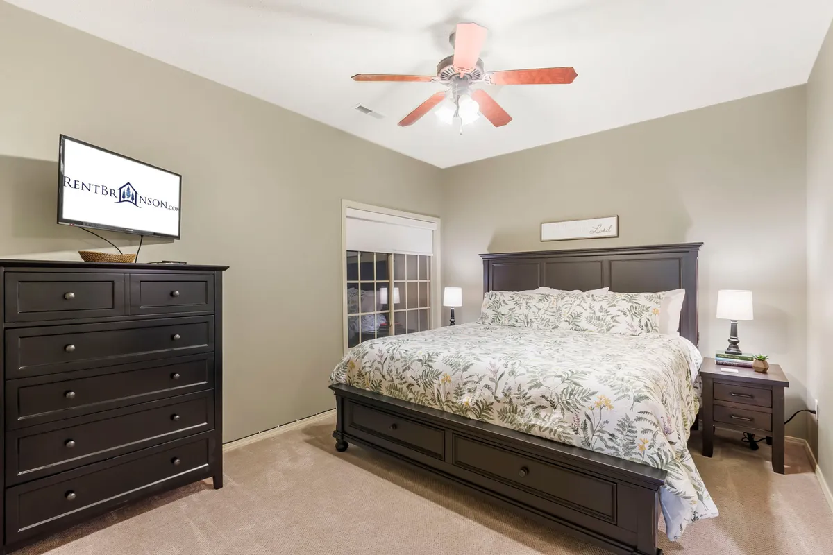 This interior image features a bedroom with a large, inviting bed, a dresser, nightstand, and wall-mounted TV. The atmosphere is relaxing, conveying a sense of comfort and privacy ideal for restful nights or quiet reading. The overall look is uncluttered and serene, supporting a restorative retreat.