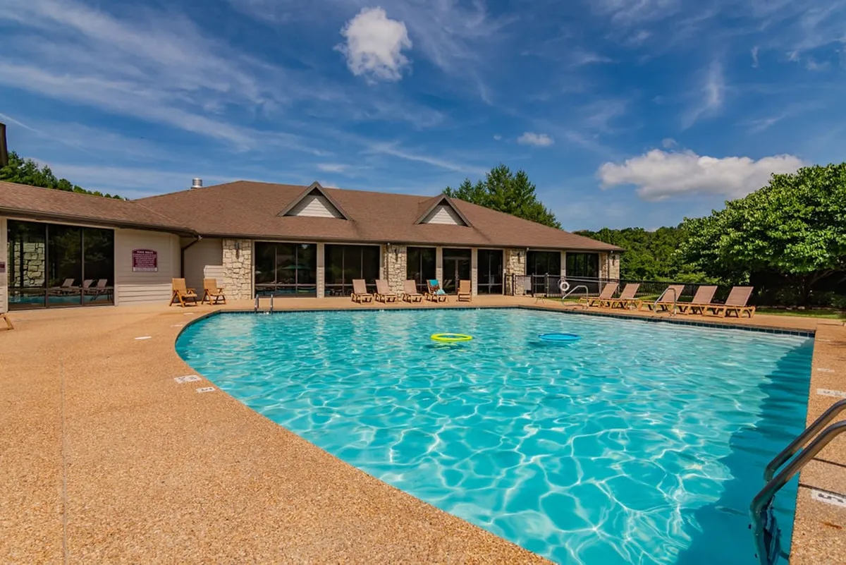 This inviting exterior features a sparkling swimming pool lined with lounge chairs, surrounded by trees and the resort building. The relaxed atmosphere suggests summer enjoyment and community interaction.