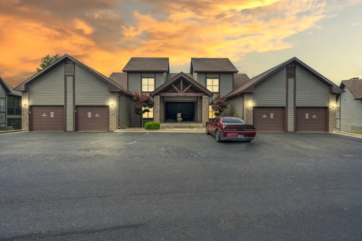 This image presents the central entrance of the building at sunset, with warm lighting, a parked red car, and decorative landscaping. The backdrop of a colorful sky sets a welcoming tone for memorable evenings and easy access to Branson nightlife.