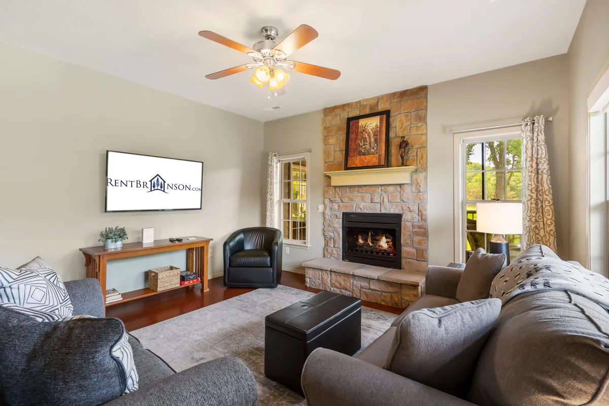 A cozy living room featuring a stone fireplace, a large flat-screen TV mounted above, comfortable seating, and decorative artwork creating a welcoming ambiance. The furnishings invite relaxation and social gatherings, with the focal point on warmth and togetherness.