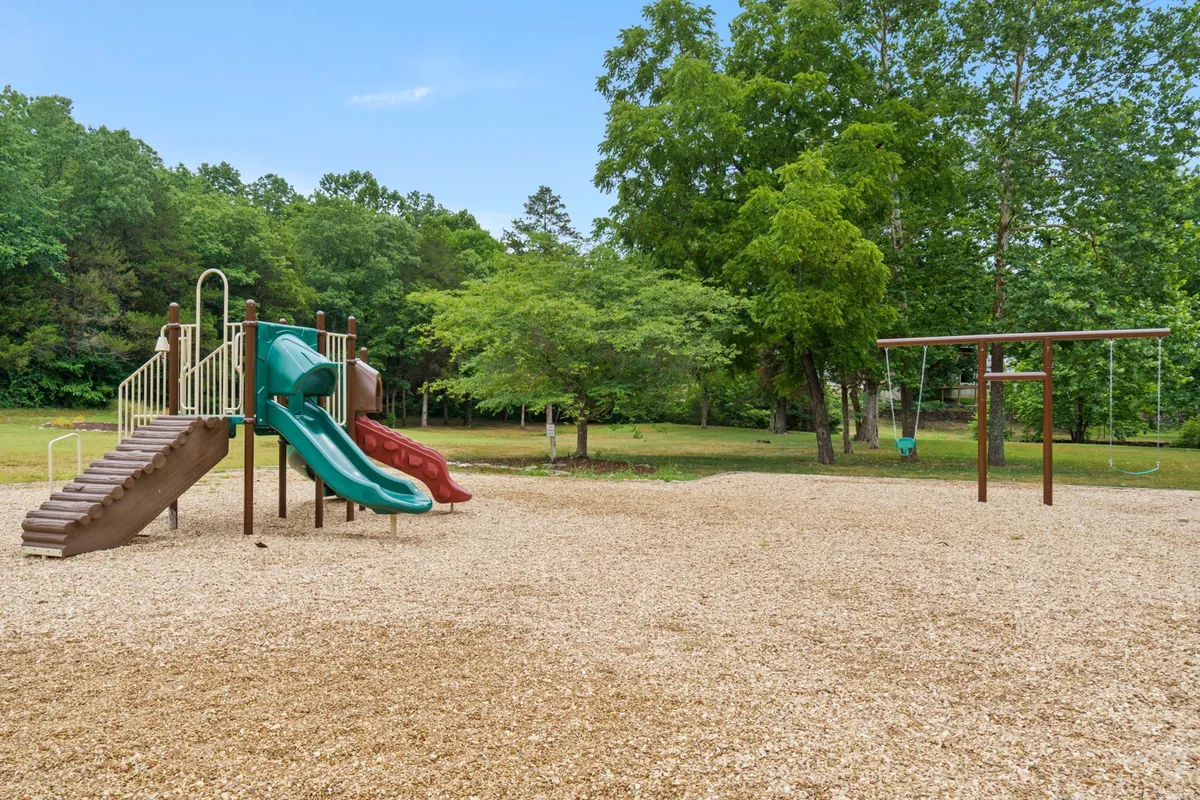This image features a vibrant playground structure with slides and a swing set, surrounded by open outdoor space. Children can be seen playing energetically, while families gather nearby for picnics and games, emphasizing the resort's family-friendly amenities.