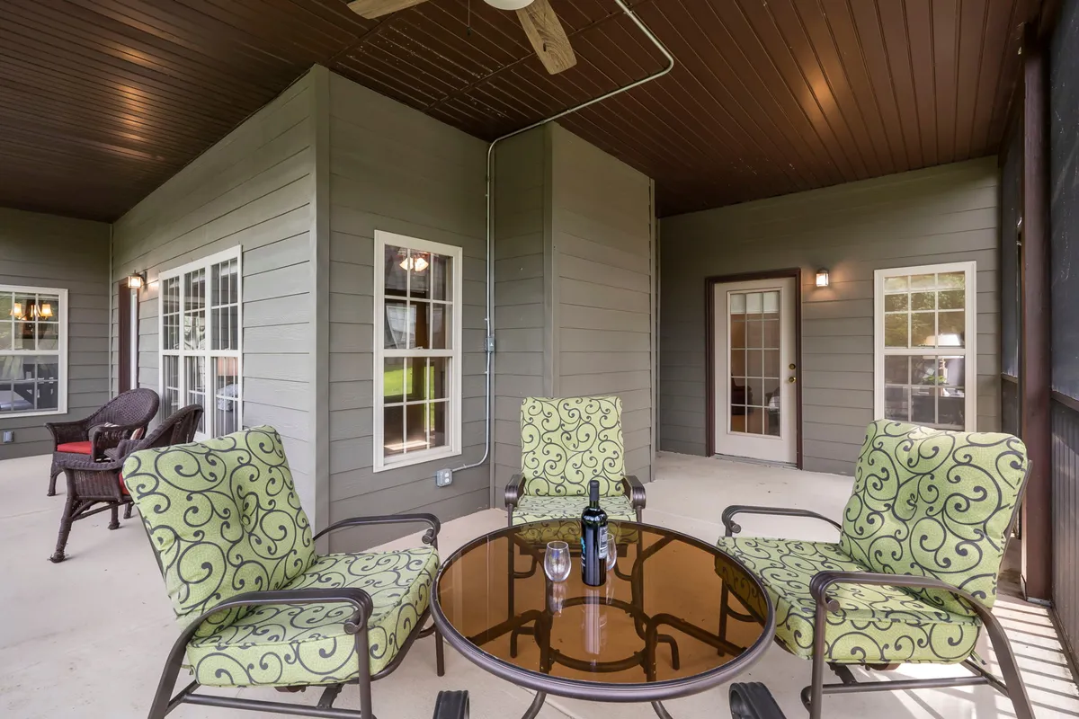 This image features an inviting outdoor seating area with a table set for drinks, decorative cushions, and large windows providing a glimpse of the home’s interior. The setting conveys relaxation, socializing, and enjoying the outdoors, perfect for sipping wine at sunset or a morning coffee in a tranquil Ozark environment.