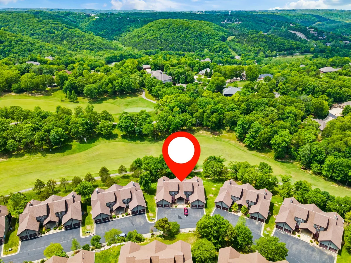 A panoramic exterior scene showing a row of attractive houses nestled in a green landscape with a hilly backdrop. The setting conveys a peaceful community vibe and suggests scenic fairway views from the property.